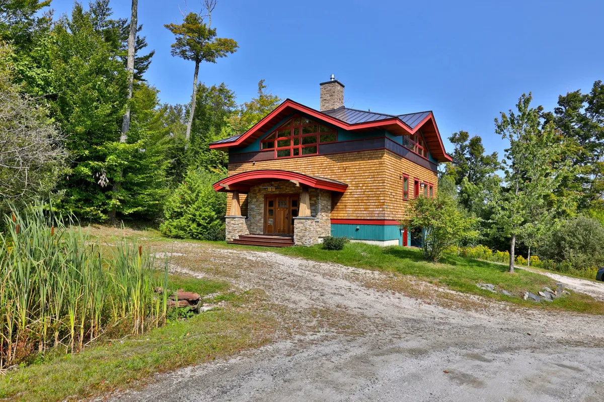 A welcoming exterior view showcases the home's distinctive roofline, stone facade, and wooden entrance door. The porch and surrounding natural setting hint at outdoor leisure, like barbecues, morning coffee with nature, or relaxing after a day’s adventures. The ambiance is warm and inviting, ideal for family gatherings and unwinding outdoors.