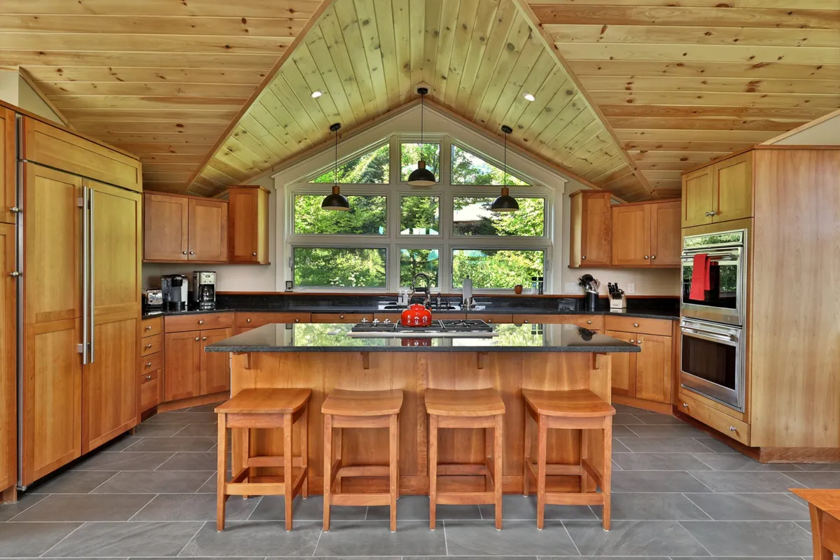 This image captures a spacious kitchen featuring a large central island, sleek modern appliances, wooden cabinetry, and generous windows that flood the area with light. The open design creates a seamless flow into adjacent living spaces, perfect for gathering and socializing.