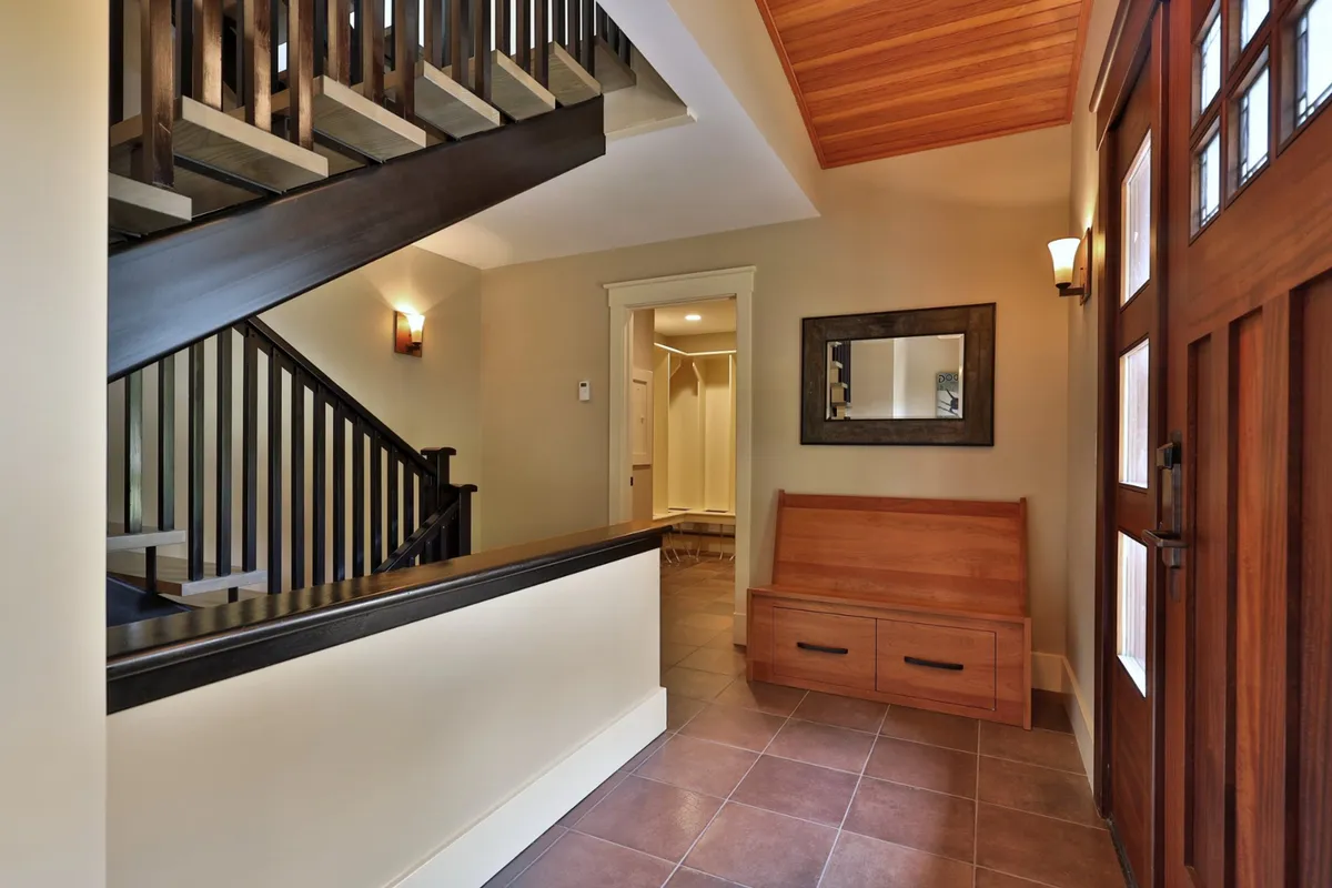 A welcoming entryway featuring a wooden bench, mirror, staircase, and front door. The space is practical for greeting guests, storing shoes, and hanging coats, setting the stage for smooth arrivals and departures.
