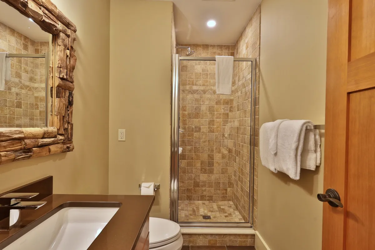 A modern, serene ensuite bathroom with a glass shower enclosure, textured tile walls, a wood-framed mirror, and a sleek sink. The ambiance is tranquil and spa-like, offering a private oasis for relaxation and rejuvenation.