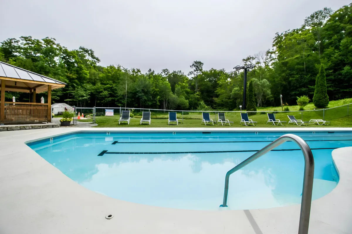 An inviting exterior shot featuring a sparkling swimming pool surrounded by lounge chairs, a gazebo, and lush greenery. The deck area and landscaping evoke a resort-like ambiance designed for relaxation and social gatherings.