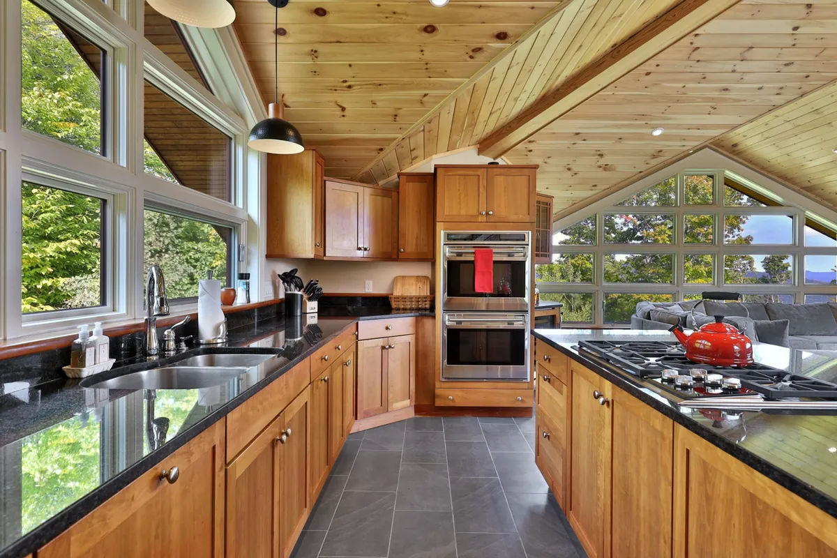 A modern kitchen with granite countertops, wooden cabinetry, and large windows, filled with natural light. The red kettle and modern appliances suggest a space ready for preparing local fare or evening cocktails.