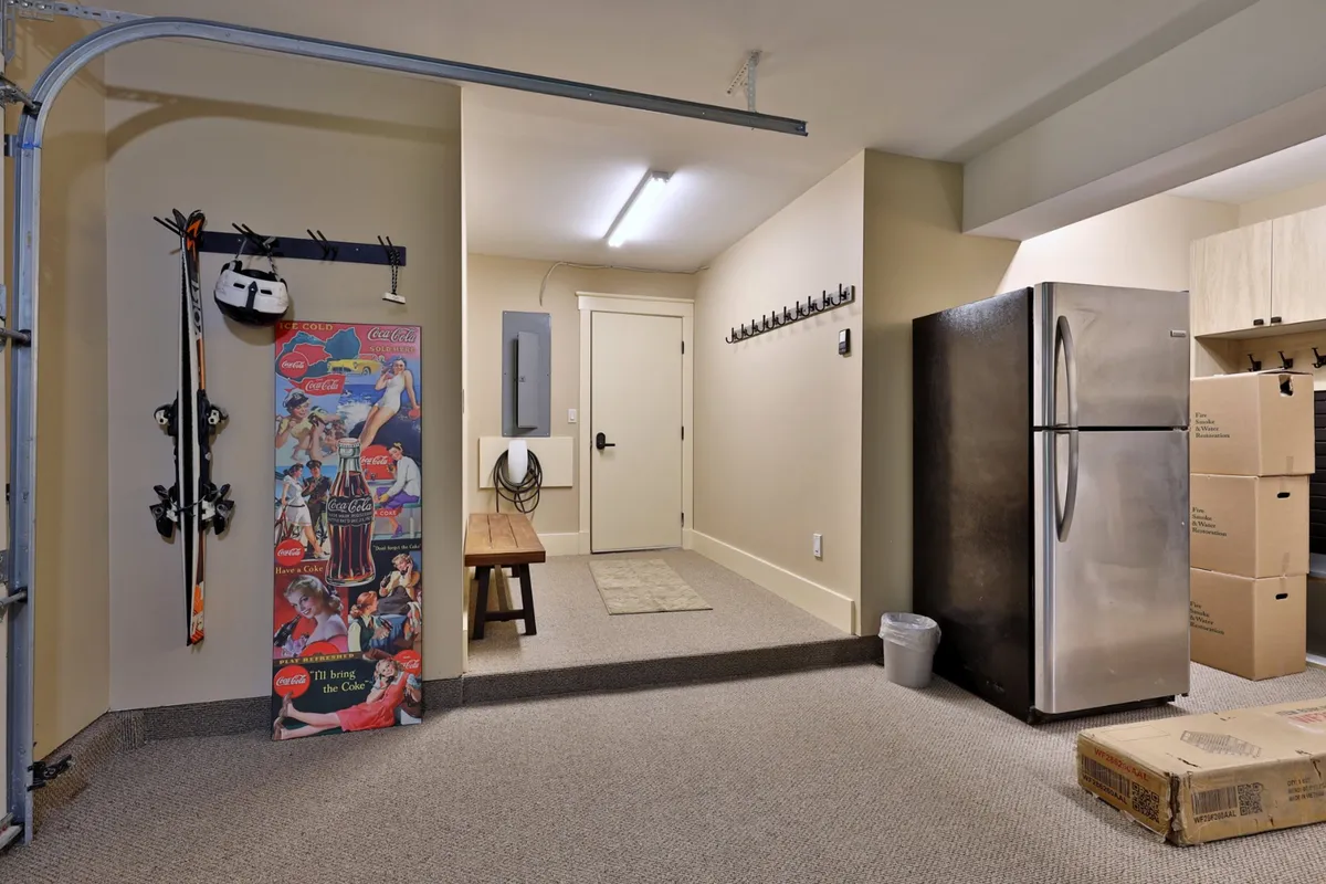 The image captures a casual gear storage area with ski equipment, a vintage poster, bench seating, and wall hooks. The atmosphere is informal and inviting, with visual cues that this is a place to prep for or unwind after skiing.