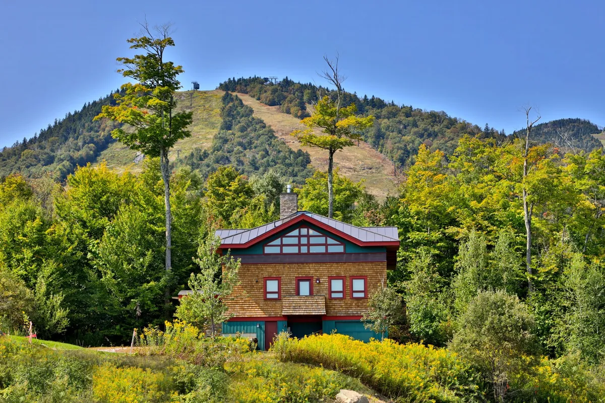 This exterior shot features the house nestled among lush greenery, with a dramatic mountain backdrop. The surrounding trees and open sky evoke a sense of freedom and connection to nature. The scene suggests opportunities for hiking, relaxing, and photography, directly referencing the Green Mountains mentioned in the section.