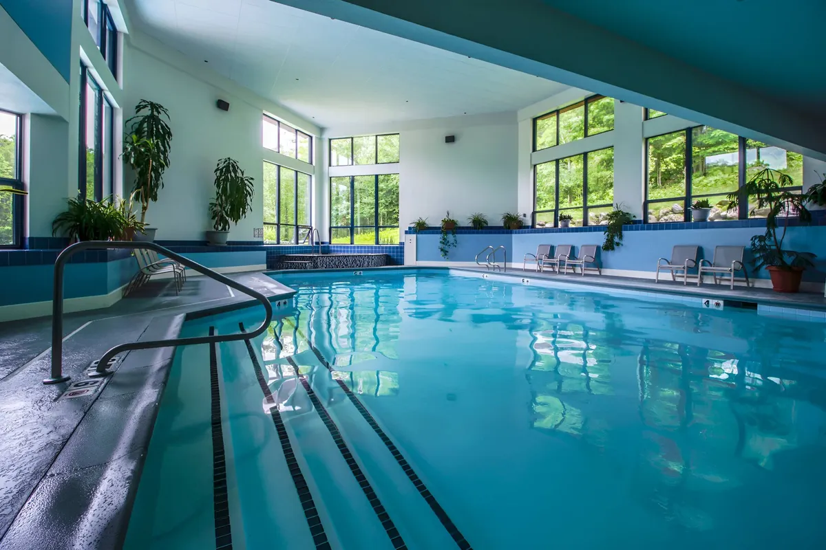 The indoor swimming pool area, complete with large windows and lush plant life, offers a serene, resort-style space to relax, swim, or socialize. The inviting water and tranquil design evoke recovery and recreation after active days outdoors.
