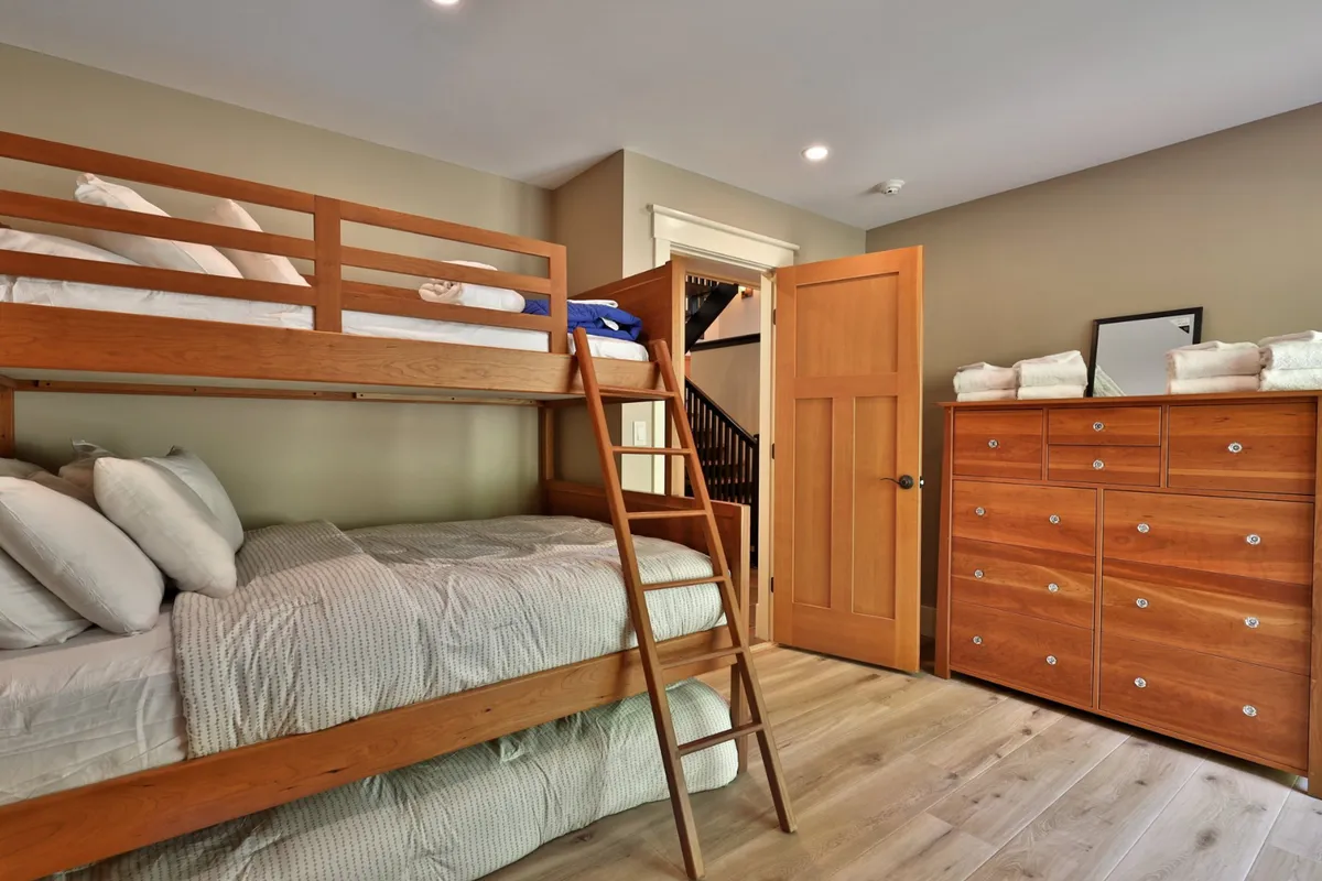 A playful bunk room with wooden bunk beds, a sturdy dresser, and an open door, designed for comfort and fun. The room radiates a sense of adventure and is ideal for older children or friends, offering both comfort and a touch of youthful excitement.