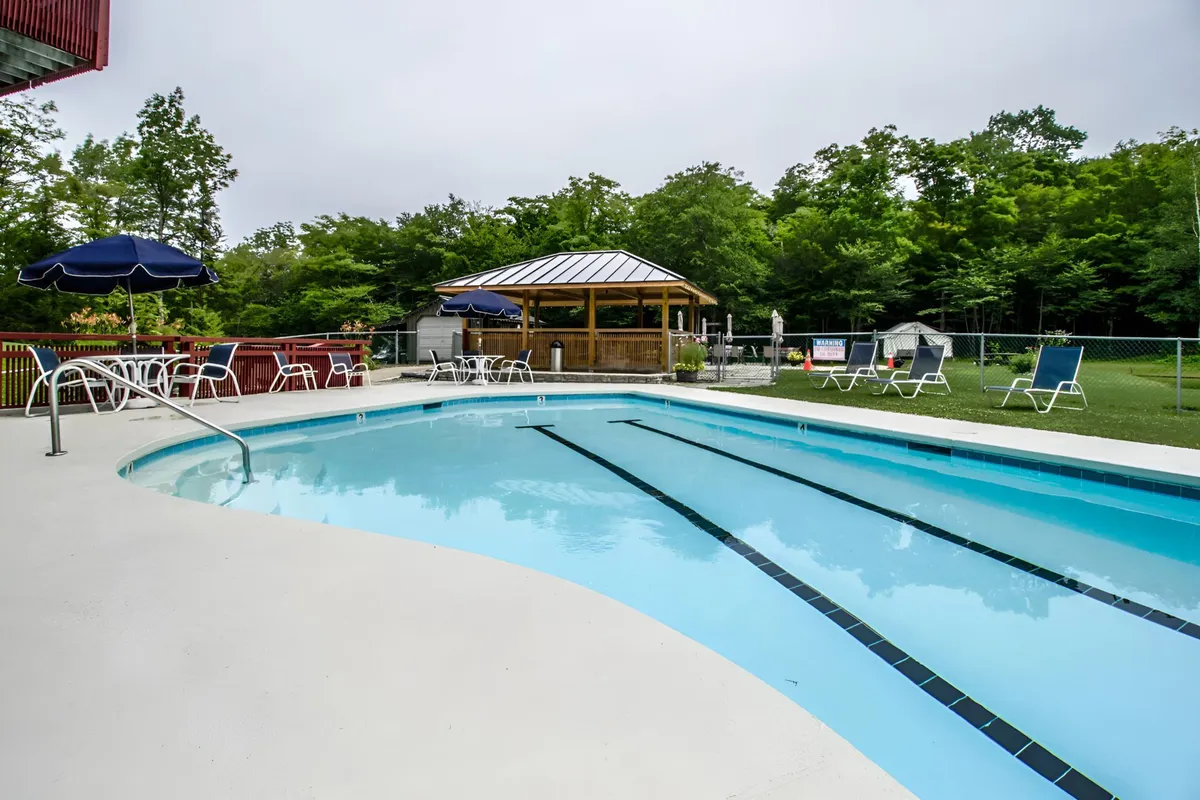 An inviting swimming pool scene with lounge chairs and a gazebo set against a backdrop of greenery. This exterior amenity signals summertime leisure, offering a place for swimming, sunbathing, and social outdoor gatherings. The space is perfect for relaxing after a day of mountain activities.